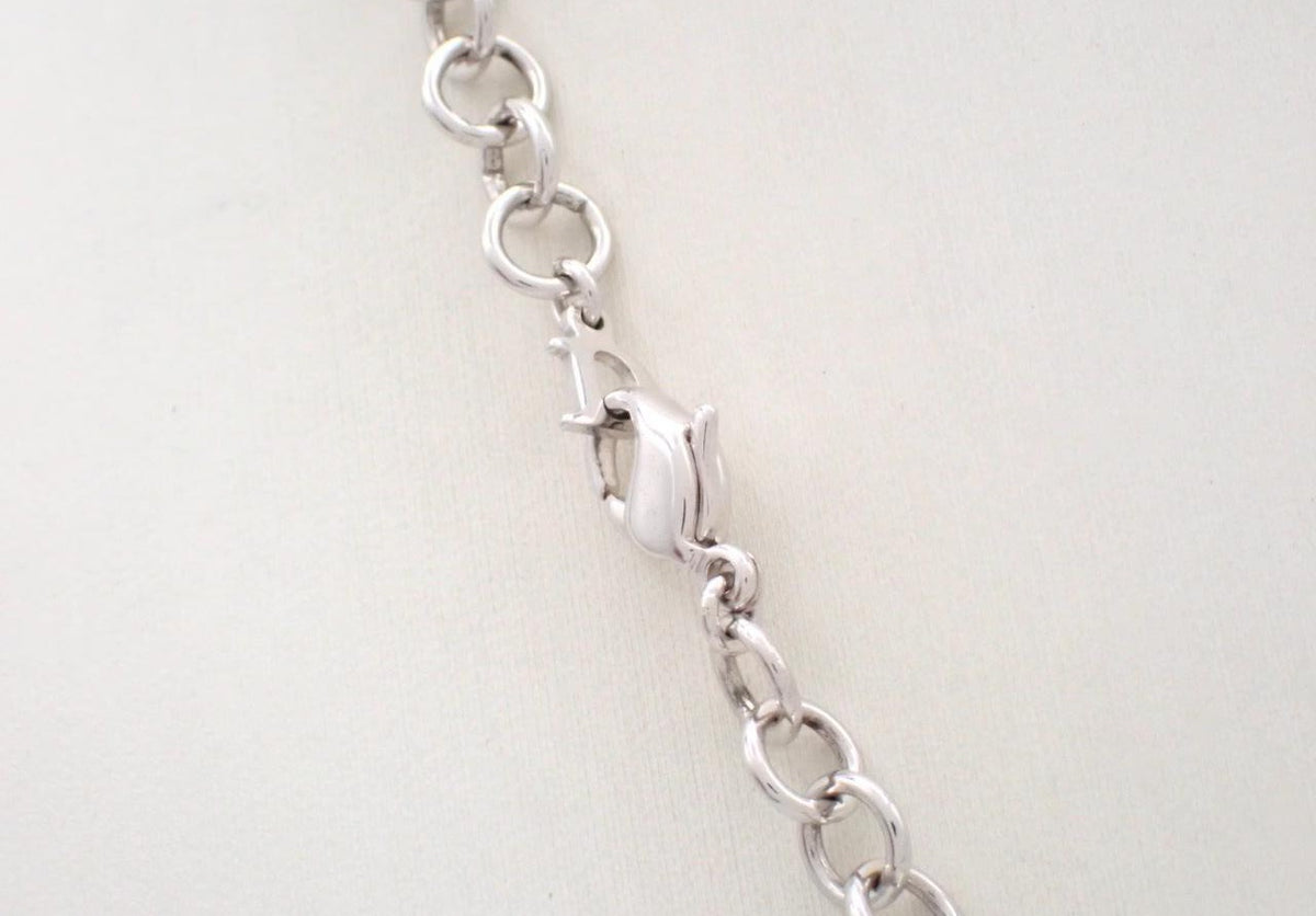 Close-up of a silver chain link bracelet showing a lobster clasp on a light beige background.